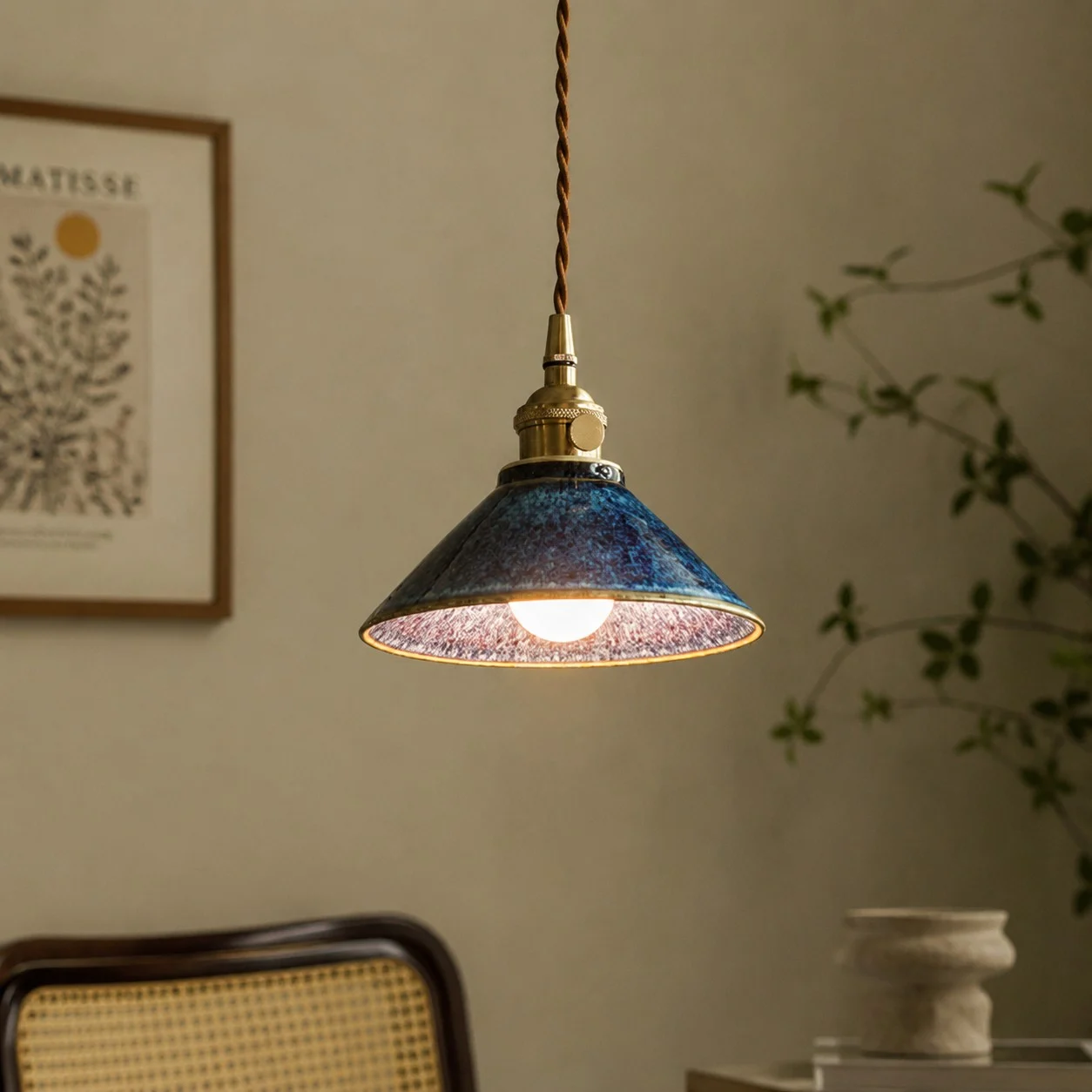 Blue ceramic pendant light beside a woven chair and wall art